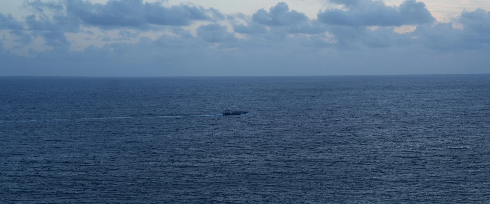 Boat crossing open water beneath a clouded sky